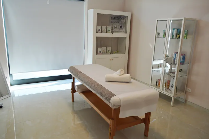 La cabina: lettino con asciugamani arrotolati, vetrina bianca dei prodotti e luce naturale